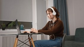 Goal-oriented girl teen freelancer working remotely typing on laptop listening to music in headphones playing computer game sitting at small table in her living room - Powered by Shutterstock - Get 15% off with code: PIKWIZARD15