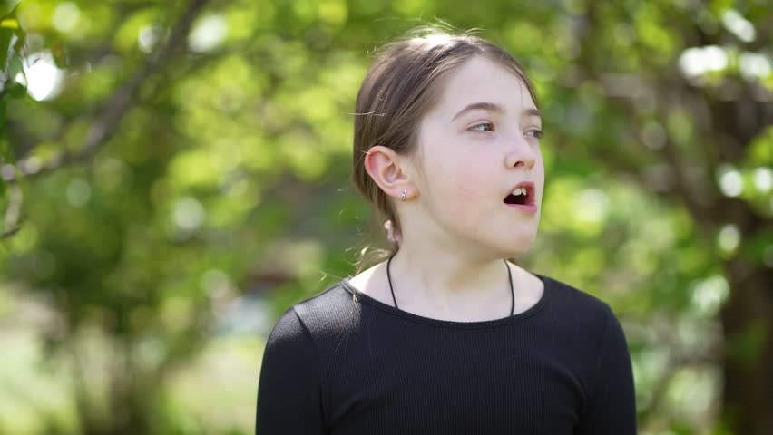 Teen Girl Shows Boredom as She Puffs Her Cheeks and Blows Air in Green Outdoor Setting During Daytime. Little cute teenage female outdoor, kid expression. Children on nature background