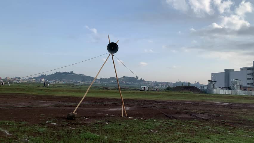 Semi-orbit drone shot circling a large speaker mounted on wood tripod in an open field during Eid Al-Adha