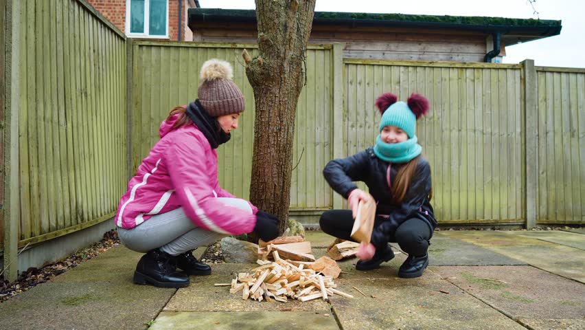 Mother and daughter playfully stacking firewood, tossing logs and arranging kindling. Fantastic family moments Spending quality time together. Woman and girl crouching near wooden pile, laughing while