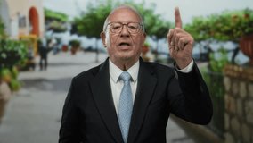 Senior man in a suit on a vibrant street points upwards, showcasing an expressive gesture in an outdoor business setting. - Powered by Shutterstock - Get 15% off with code: PIKWIZARD15