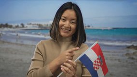 Young woman smiling and pointing to a croatian flag at the seaside, capturing a vibrant beach day with waves and blue sky. - Powered by Shutterstock - Get 15% off with code: PIKWIZARD15