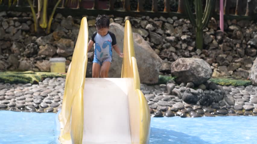 Little boy play joyfully on a yellow slide in an outdoor pool Surrounded by greenery and rocks, hid splash and laugh under the sun, embodying summer fun and adventure
