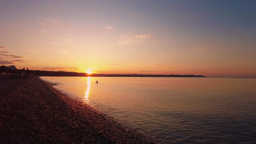 4K A peaceful scene of a lone swimmer enjoying the calm waters of the Mediterranean Sea during a golden sunrise on Konyaalti Beach in Antalya, Turkey