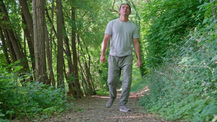 A man is savoring a delightful and peaceful walk along a picturesque forest trail that is surrounded by lush greenery. Slow motion