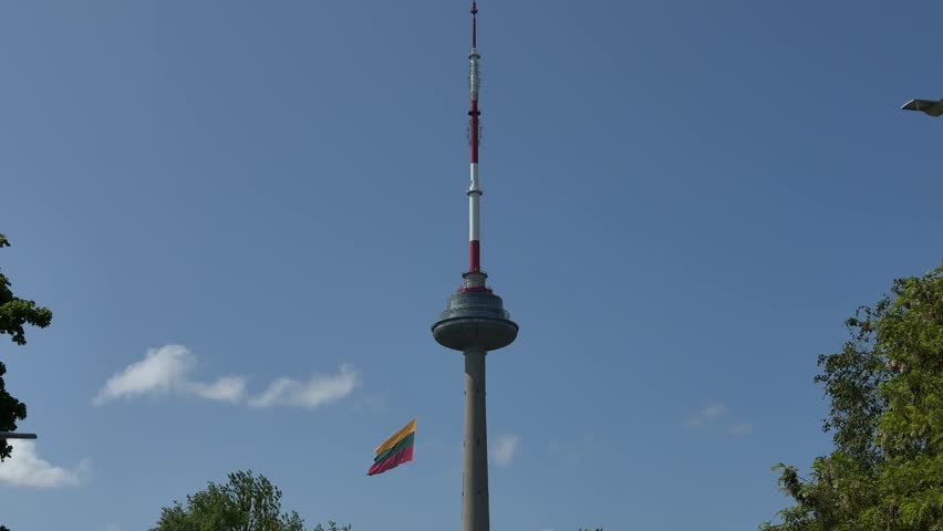 Lithuanian flag waving at TV Tower in Vilnius. Tower structure rises against a clear blue sky, featuring vibrant flag fluttering nearby, symbolizing national pride and identity