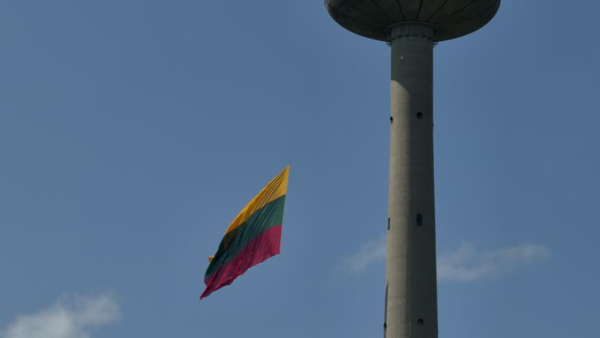Lithuanian flag waving at TV Tower in Vilnius. Tower structure with vibrant flag waving against clear blue sky, symbolizing national pride and identity in a serene urban landscape
