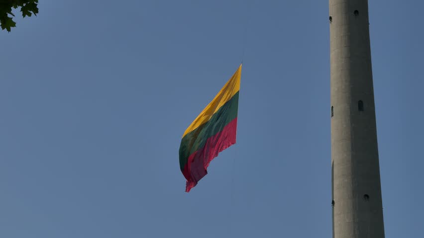 Lithuanian flag waving at TV Tower in Vilnius. Tower structure rises against clear blue sky, showcasing vibrant flag fluttering in the wind, symbolizing national pride and identity