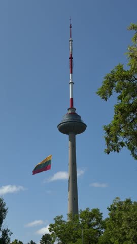 Lithuanian flag waving at TV Tower in Vilnius. Tower structure rises against a clear blue sky, adorned with a vibrant flag, symbolizing national pride and identity in a serene urban landscape
