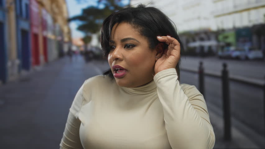 Woman listening intently on an urban street as a plus size latina stands outdoors engaged in conversation amidst city buildings and traffic.