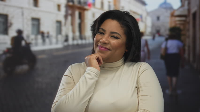 Woman smiling outdoors on city street in an urban setting, featuring a young, plus size, hispanic, latin, female with thoughtful expression.