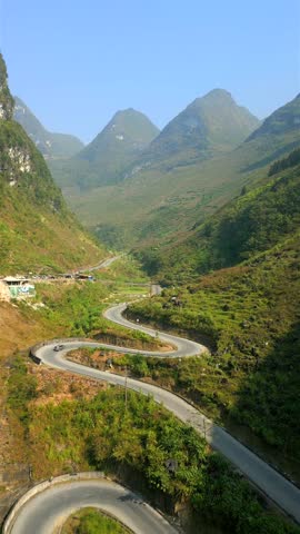 Aerial view of car driving on winding mountain road in Ha Giang Loop, Vietnam. Serpentine path through lush green hills and limestone peaks in remote northern Vietnam.