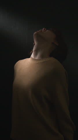 Vertical shot of young depressed red-haired woman gazing upward and screaming in shadow with dramatic lighting