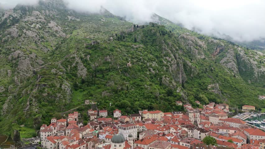 Aerial drone view of Kotor Old Town Stari Grad in Montenegro. Moody misty mountains and blue waters Fjord UNESCO heritage ancient city. European travel holiday.