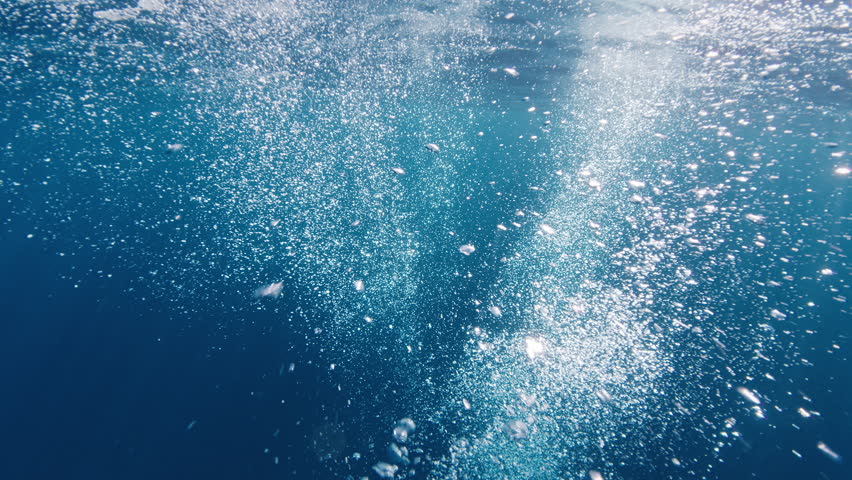 Underwater view of the sea surface and bubbles from divers. Camera flies through the cloud of bubbles in the sea