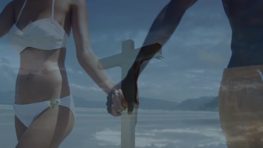 camera tilting upward revealing cross graphic behind couple walking shore for travel marketing. Romance, shoreline, unity, serenity, spirituality, leisure, nature