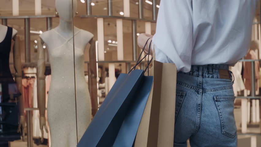 Close-up scene of a female customer examining clothing through the window of a fashion store inside a shopping center.
