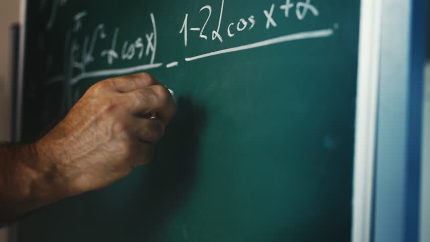 Male math teacher writing equations on chalkboard during university lecture