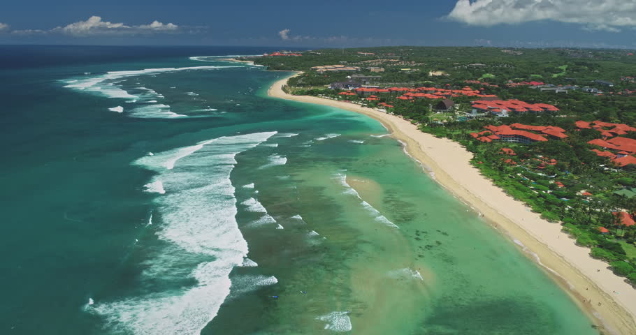 Stunning aerial view of Nusa Dua beach with breaking waves and luxury hotels along the coast meeting the turquoise water of the Indian Ocean in Bali, Indonesia