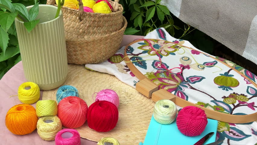 A cozy outdoor corner for creativity in a summer garden: a cushioned swing serves as a relaxing seat for embroidery, surrounded by lush greenery and flowers. Nearby stands a small table with colorful 