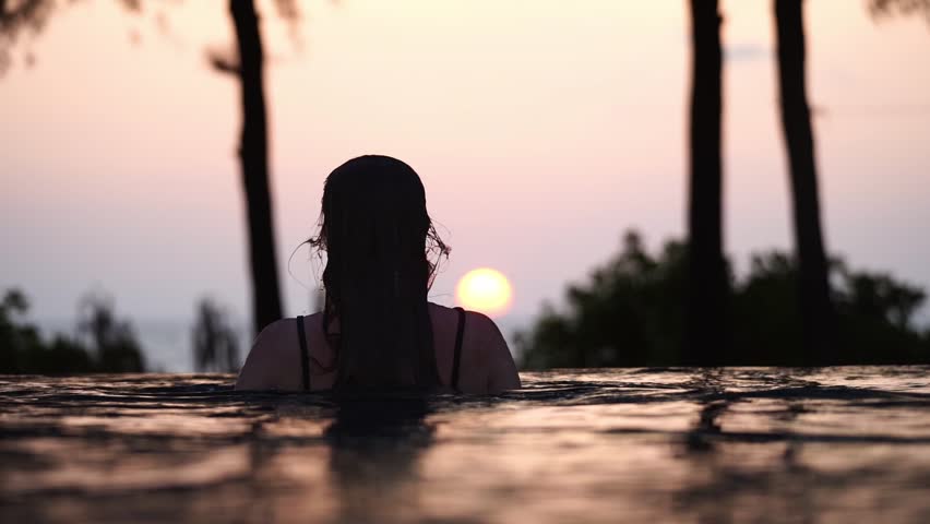 Woman bathing in a pool by the sea at sunrise or sunset