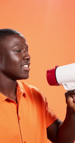 Black man, bullhorn and shout for announcement in studio with voice, deal and sale by orange background. Person, loudspeaker and profile with space, fashion and info with promotion for launch