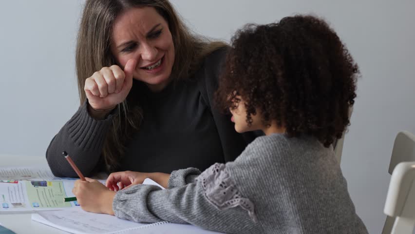 Caucasian mother and African American daughter studying at home, doing homework in cosy white room. Parent teach, child school girl learn knowledge, write exercise read book. Education for children