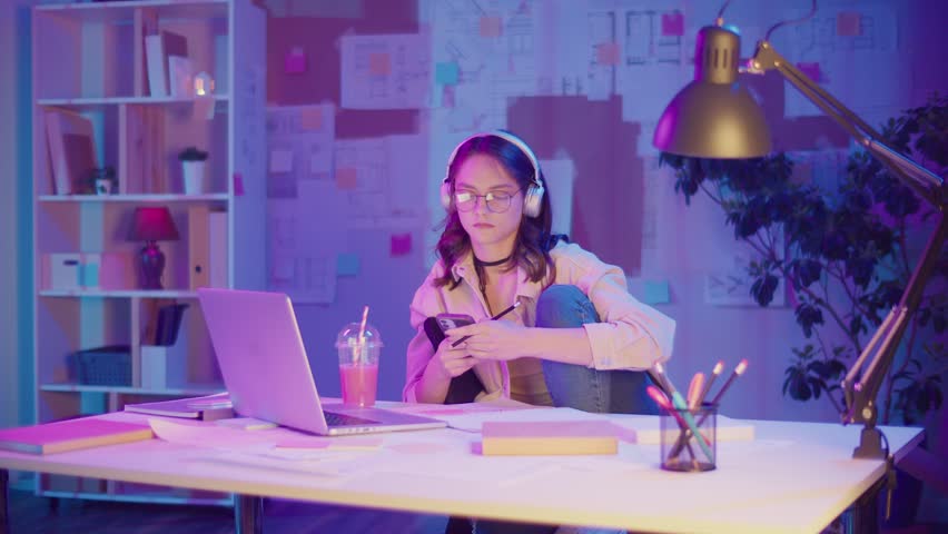 Gen Z Lifestyle, Digital Multitasking, Neon Mood. Teen Girl Draws While Listening Music and Watching Laptop Screen. Personal Expression in Creative Chaos of Modern Youth in Neon Light