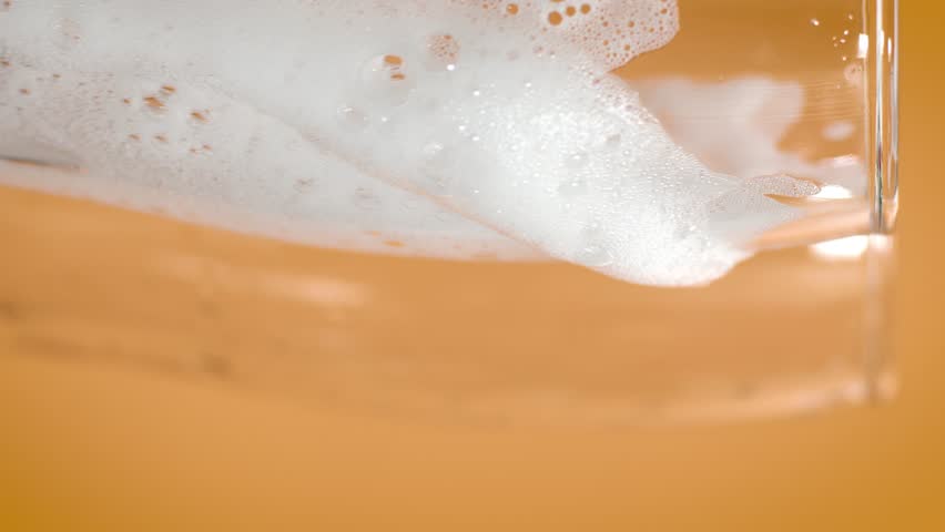 Foam of dishwashing liquid sliding down glass surface on orange background, showing white detergent bubbles in motion for cleaning, hygiene, and product visuals.