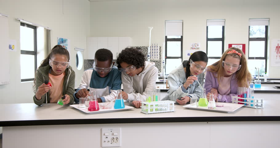 In school, kids wearing safety goggles experimenting with colorful liquids in science class. chemistry, education, children, laboratory, investigation, discovery