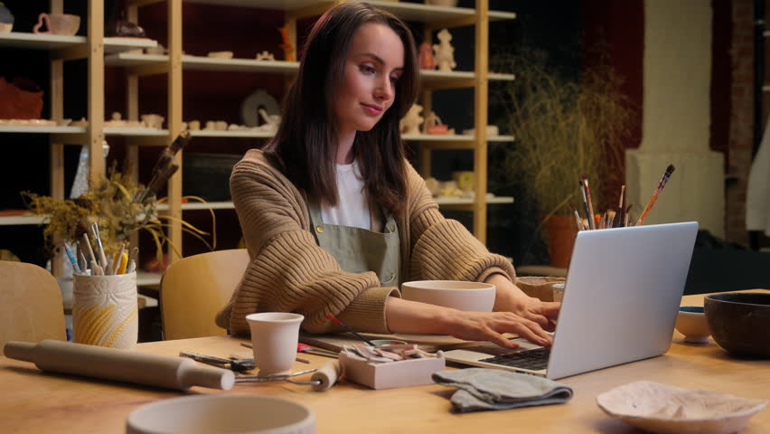 Caucasian woman small business owner saleswoman laptop working online sales ceramics craft store crockery handmade bowl female girl artist potter sculptor artist online shopping in pottery workshop
