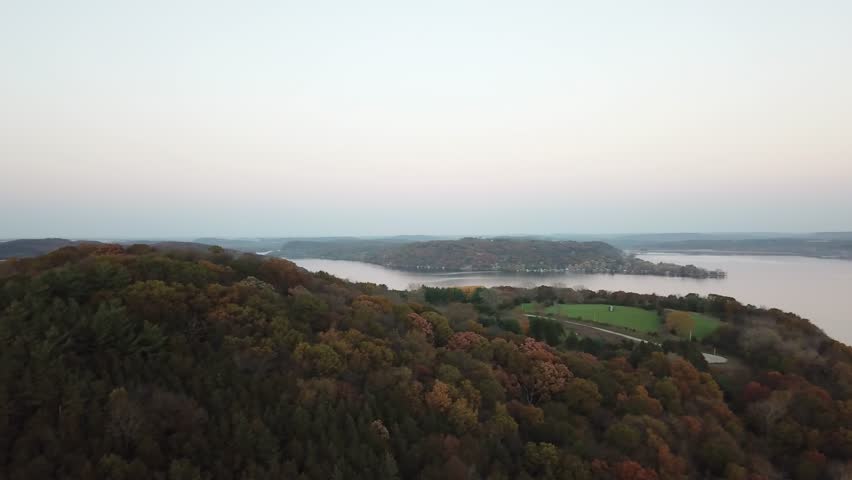 A peaceful aerial view of Lake Wisconsin at dusk, with calm water stretching alongside wooded shoreline and autumn-colored trees. A serene landscape blending twilight tones and seasonal charm.