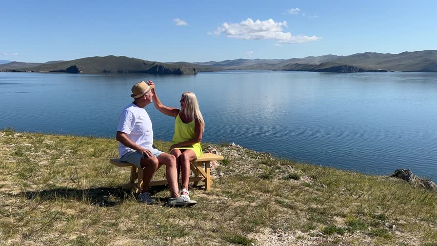 A man and woman walk along the lake under a clear sky, enjoying the warmth of the sun and beautiful nature.