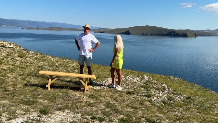 A man and woman walk along the lake under a clear sky, enjoying the warmth of the sun and beautiful nature.