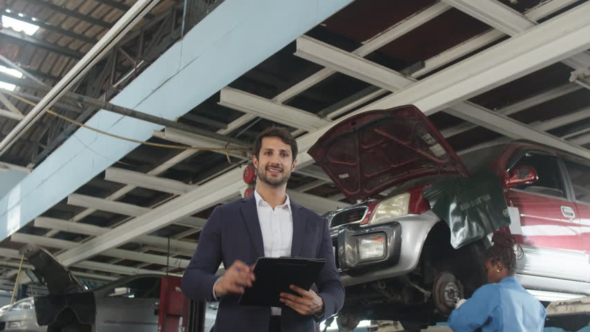Portrait of Hispanic male mechanic manager smiling, arms crossed, cheerful, and looks at camera, service insured claim business, car fix warranty and maintenance at automotive garage station industry.