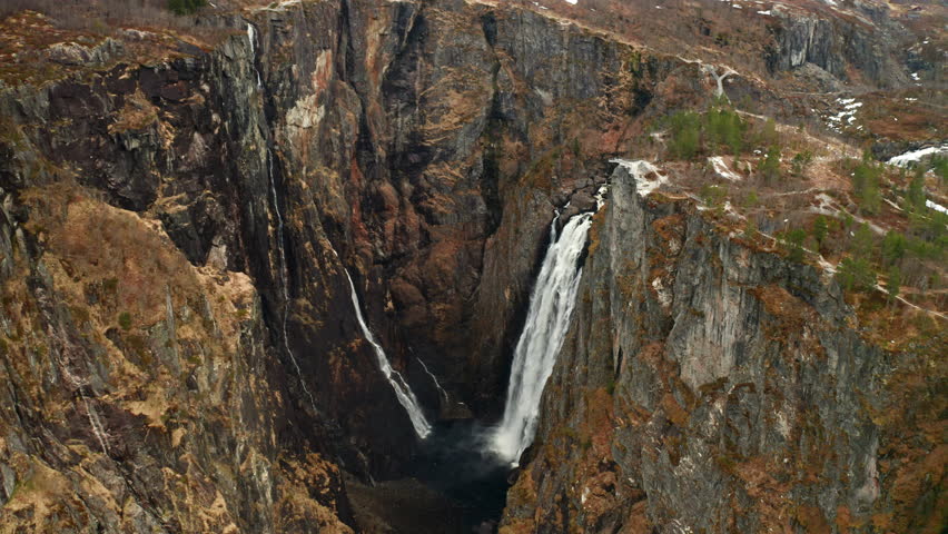 Powerful Voringsfossen waterfall with cascades plunging dramatically into gorge below. Steep cliffs emphasize sheer scale and raw beauty of Norway