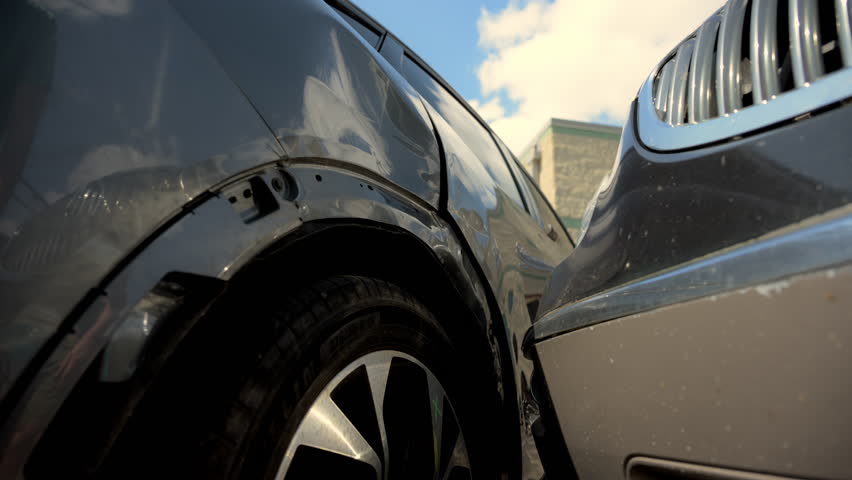 The owner is observing the damages after a car crash accident scene with two cars on the street road. Close up view of damaged elements. 