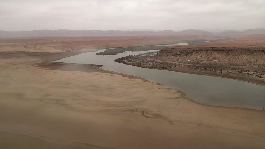 Drone view flying along the coast where the desert meets the ocean, showing a river mouth and foggy, desolate landscape near Tan-Tan, Morocco