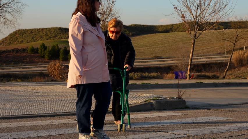 Pregnant woman helping elderly lady cross street with walker, sunny afternoon mood