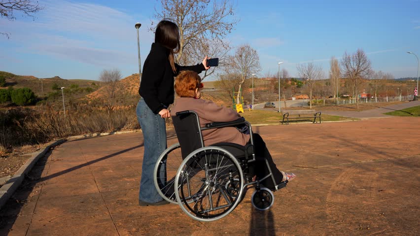 Granddaughter takes a selfie with her granny in wheelchair on a sunny day