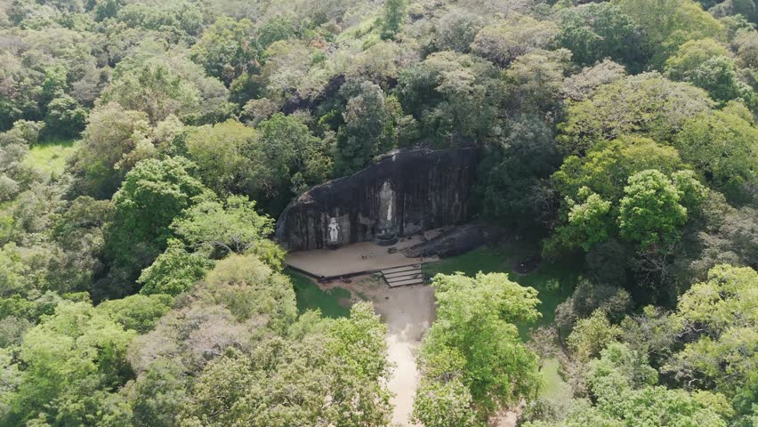 Buddha carvings on remote rock face in Sri Lanka jungle. Drone dynamic spiral zoom in.