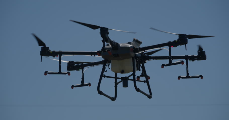 Aerial drone flying over a cultivated farm field during a crop monitoring or spraying mission, highlighting advanced agricultural technology and precision farming techniques in rural settings.