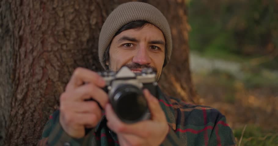 Hiking guy takes a camera brings it to his face and takes a photo. Portrait of a guy taking a photo looking at the camera in a forested area during a hike