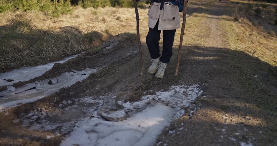 Person in hiking clothes steps onto frozen water on a dirt path during a hike outside of an urban area. Winter hike
