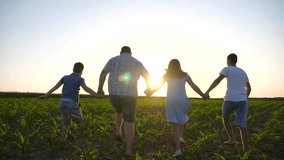Happy family with children running through cornfield holding hands of each other at sunset. Young couple of parents with two sons jogging among green meadow and enjoy to spending time together - Powered by Shutterstock - Get 15% off with code: PIKWIZARD15