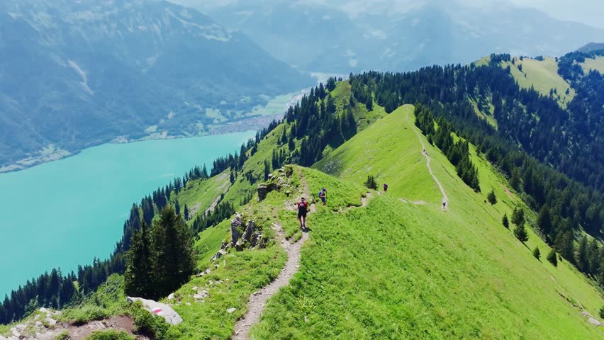 Man and woman descend narrow Swiss alpine ridge trail with turquoise lake views