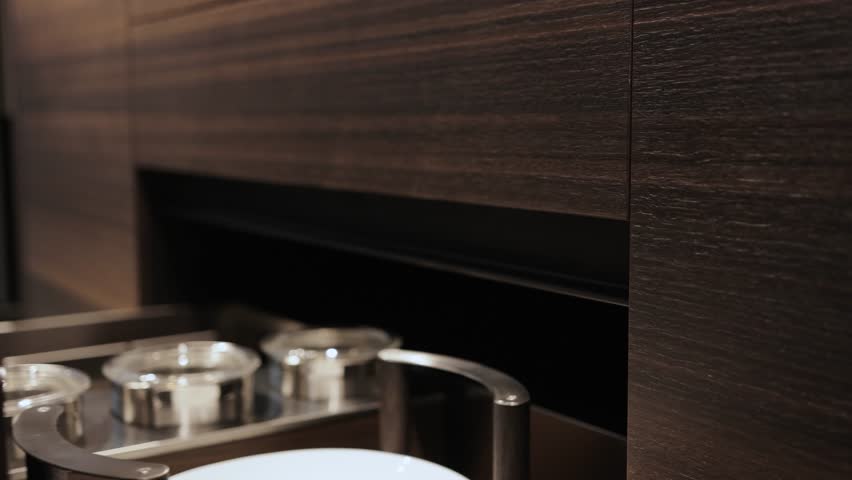 Close-up, female hand closing drawers of dark modern kitchen cabinets and showing dishes inside. Kitchen island, modern kitchen interior design.