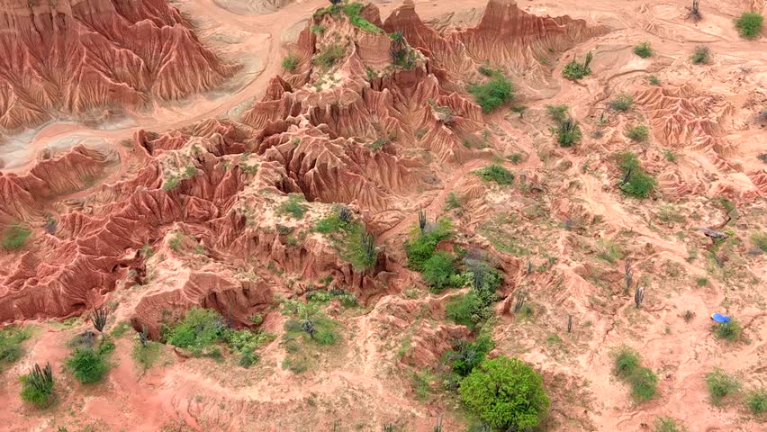 Close-up aerial view of Tatacoa Desert's stunning red formations and sparse vegetation, illuminated by warm sunlight. Captured from above, it highlights the striking natural textures.