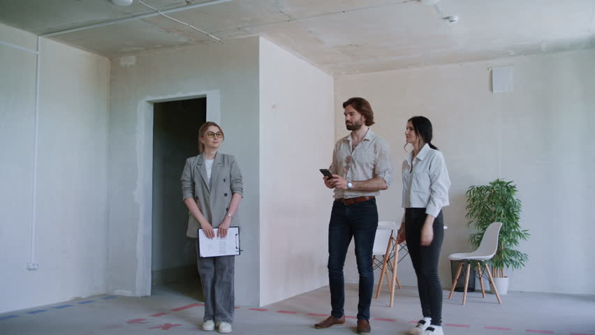 Young couple tours a new, unfurnished apartment with a real estate agent, capturing details on their mobile phones while exploring the space