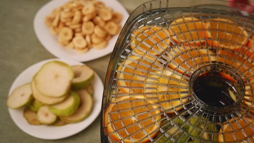 Woman carefully arranging pear slices onto a dehydrator tray, alongside other fruits like oranges and bananas, for healthy snack preparation